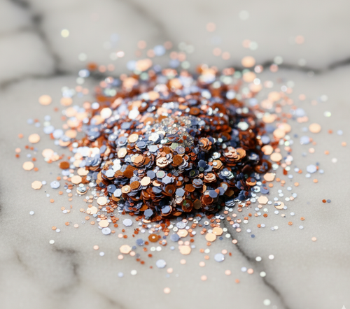 Close-up of Loose Cosmetic Bioglitter® EU Microplastic Legislation Compliant Bundle (M–L sizes) showing mixed copper, silver, and blue biodegradable glitter on marble surface.